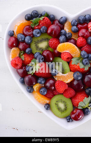 Regenbogenfarbenen Früchte wie Himbeeren, Erdbeeren, Kirschen, Heidelbeeren, Mandarinen und Kiwis im Herzen gestalten Schüssel Stockfoto