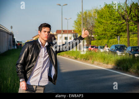 Hübscher junger Mann, ein Tramper warten Auto am Straßenrand in der Stadt, tragen schwarze Lederjacke Stockfoto