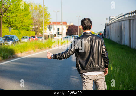 Rückseite des jungen Mann, einen Tramper warten Auto am Straßenrand in der Stadt, tragen schwarze Lederjacke Stockfoto