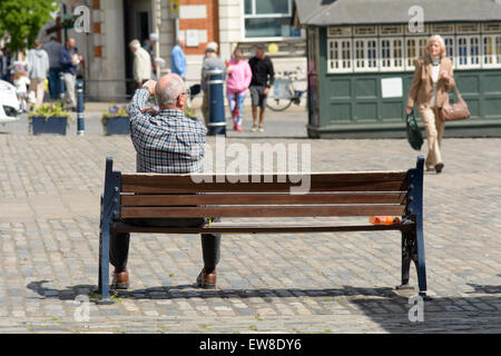 Mann saß auf der Bank in der Sonne Old Market Square Hitchin Hertfordshire England Stockfoto