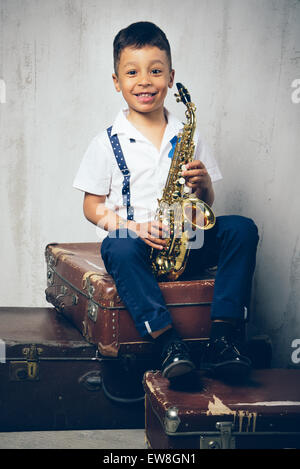sechs Jahre alter Junge sitzt mit Saxophon auf Retro-Koffer Stockfoto