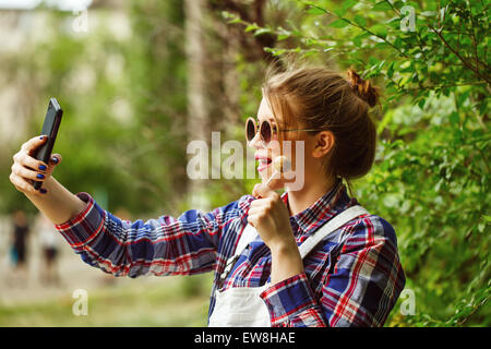 Teengirl mit ein Foto von sich mit Smartphone. Selfie Stil Bilder. In warmen Farben getönt. Mädchen mit einem Lutscher. Stockfoto