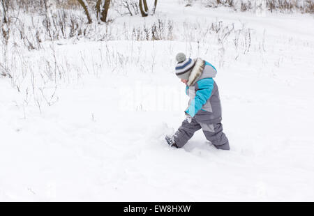 kleiner Junge in Overall und Mütze Spaziergänge im Schnee Stockfoto