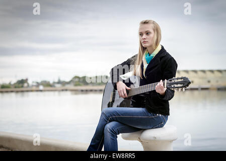 Schöne blonde Mädchen sitzen auf der Bitt und Gitarre zu spielen Stockfoto