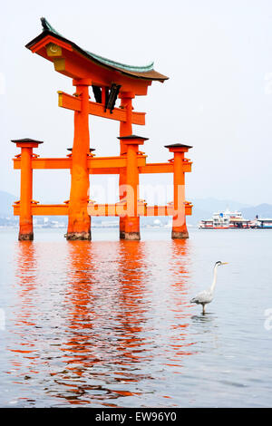 Eine der ikonischen japanischen Sehenswürdigkeiten, der Große Torii auf der Insel Miyajima. Umgeben vom ruhigen Meer mit einem einzigen Reiher im Vordergrund. Stockfoto