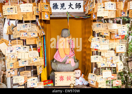 Japan, Miyajima, Daisho-in-Tempel. Bibbed Jizo-Statue auf dem Sockel in einem kleinen Schreingehäuse mit Massen von hängenden ema-Bretter auf beiden Seiten. Stockfoto