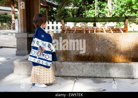 Kaukasier Kind, Junge, 5 Jahre alt, trug Japanische blauen Kimono und hält mit beiden Händen einen Sensu gefaltet Ventilator. Steht die Reinigung Becken an Schrein. Stockfoto
