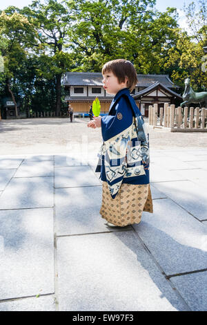 Japanese-Caucasian Kind, Junge, 5 Jahr alt, trägt blaue Kimono, wandern durch Schrein Innenhof, während eine mit grüner Hintergrundbeleuchtung Blatt. Stockfoto