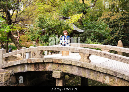 Japan, 5 Jahr alt, Kaukasier Kind, Junge, im Kimono, Wandern auf Schrein Brücke und halten sensu, Ventilator, in beiden Händen. Für 3-5-7 Zeremonie gekleidet. Stockfoto