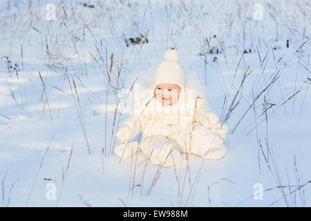 Lustige Baby spielt mit Grass in ein Schneefeld an einem sonnigen Tag Stockfoto