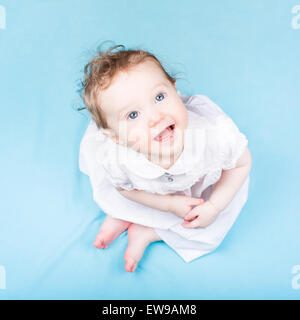 Wunderschönes kleines Mädchen in einem weißen Kleid auf einer blauen Decke Stockfoto