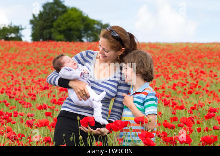 Junge Mutter mit ihrem Sohn und Neugeborenen Baby in eine schöne rote Blumenfeld Stockfoto