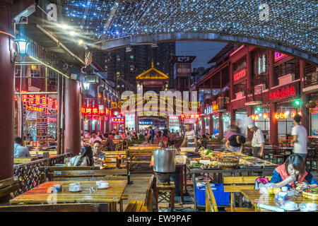 Menschen, die draußen in einem neonbeleuchteten Innenhof essen, umgeben von Restaurants in Chengdu, China Stockfoto