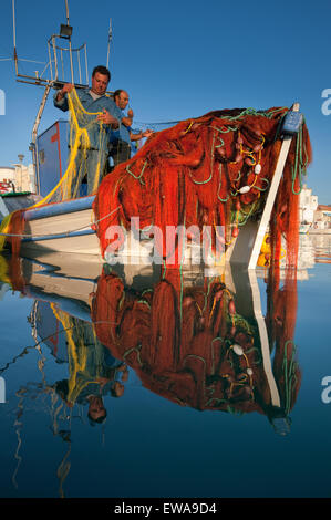 Fischer Instandsetzung rot Fischernetze auf lemnos oder Limnos Island, Griechenland. Boot und roten Netzen auf Meer Wasser wider. Von Myrina Quay. Inseln des Ägäischen Meeres. Stockfoto