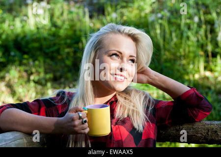 schöne blonde Landmädchen aus einem gelben Becher trinken Stockfoto