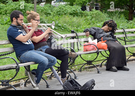 Ein junger Mann und eine Frau spielen ihre Trompeten im Washington Square Park in New York während eine schlafende Frau blind gegenüber der Lärm ist. Stockfoto