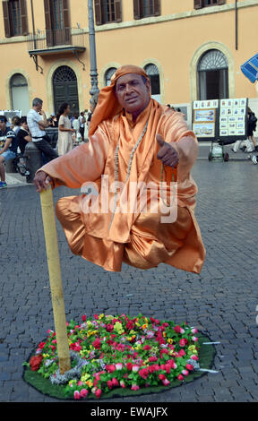 Ein Straßenmusikant in einer orangefarbenen Robe scheint im Austausch für Spenden zu schweben. Auf der Piazza Navona in Rom, Italien. Stockfoto