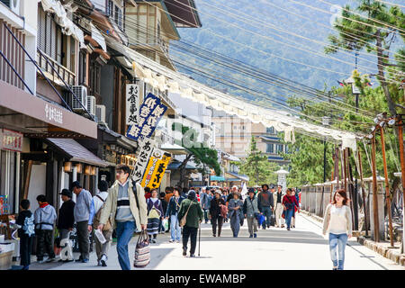 Touristen gehen unter Sonnenschirmen über eine Straße mit Souvenierläden an die touristische Attraktion der Insel Miyajima in Japan gefüllt gezogen. Stockfoto