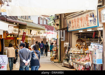 Touristen gehen unter Sonnenschirmen über eine Straße mit Souvenierläden an die touristische Attraktion der Insel Miyajima in Japan gefüllt gezogen. Stockfoto