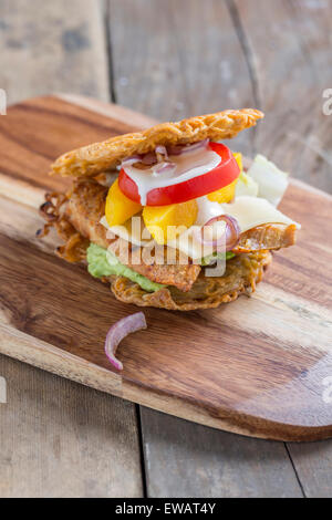 Burger gemacht von asiatischen Ramen-Nudeln mit Huhn Mango Tomaten Käse, roten Zwiebeln und Avocado Creme auf einem rustikalen Holztisch Stockfoto