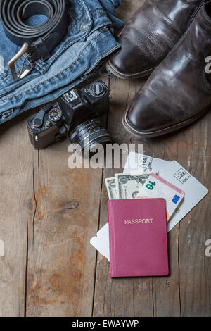 Jeans, Gürtel, Lederstiefel, Vintage-Kamera und Reisepass, Tickets und Geld auf einem rustikalen hölzernen Hintergrund Stockfoto