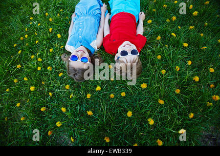 Unbeschwerte Freunde in Sonnenbrille liegt auf grünen Rasen mit Löwenzahn Stockfoto