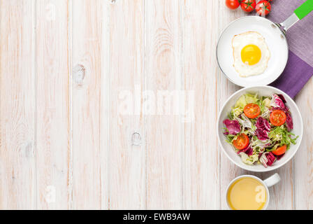 Gesundes Frühstück mit Spiegelei, Tomaten und Salat auf weißer Holztisch. Draufsicht mit Textfreiraum Stockfoto