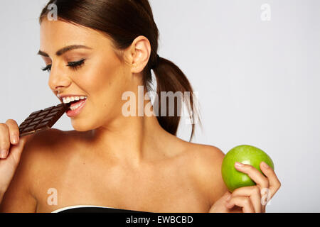 Sportliche Frau Wahl zwischen gesunden Apfel und Schokolade Stockfoto