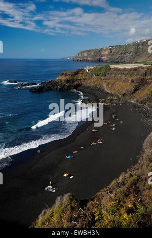 Die Badenden liegen an einem schwarzen Sandstrand vulkanischen Ursprungs am Strand Playa El Bollullo in einer abgeschiedenen Bucht östlich der Stadt Puerto de La Cruz im Norden Teneriffas; eine der kanarischen Inseln des spanischen Archipels vor der Küste Nordwestafrikas. Stockfoto