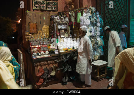 Ein Mann verkauft Mützen und religiöse Gegenstände in einem street Shop in Chandni Chowk, Alt-Delhi, Indien. Stockfoto