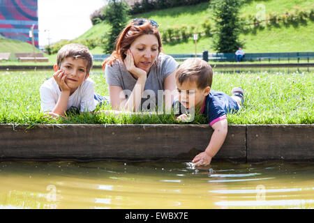 Porträt der Mutter mit zwei Kindern liegen auf dem Rasen am Ufer eines Teiches Stockfoto