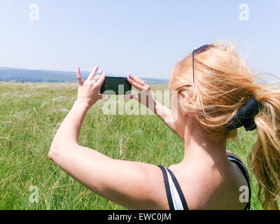 Junge weibliche Fotografen fotografieren im Freien. Frau mit Handy oder Kamera im Bereich fotografieren Natur, Feld, Wiese und Stockfoto