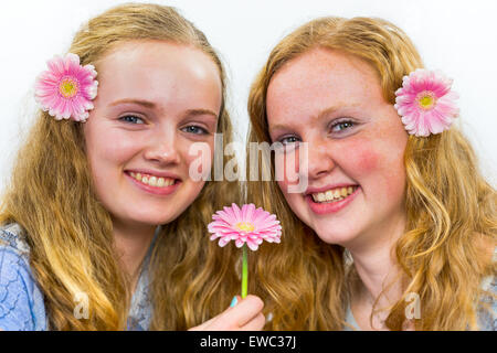 Zwei kaukasische Mädchen im Teenageralter lachend mit rosa Blüten in langen Haaren isoliert auf weißem Hintergrund Stockfoto