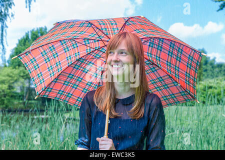 Kaukasische Teenager-Mädchen hält Regenschirm an regnerischen Tag in der grünen Natur Stockfoto