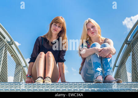 Zwei niederländische Teenager Freundinnen sitzen auf Metallbrücke mit blauem Himmel Stockfoto