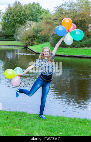 Kaukasische Teenager-Mädchen am Teich im Park mit bunten Luftballons Stockfoto