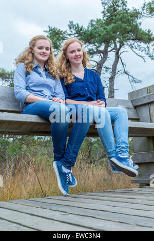 Zwei niederländische Mädchen sitzt auf einer Holzbank in der Natur Stockfoto