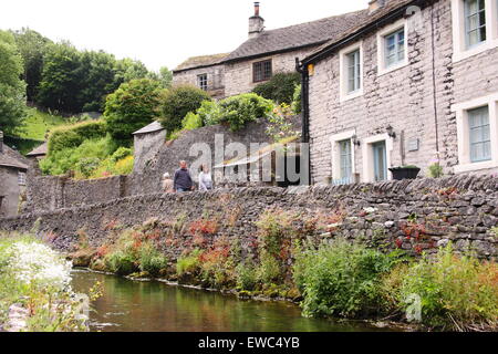 Wanderer passieren einer Trockensteinmauer auf Peakshole Wasser im Herzen von Castleton Dorf im Sommer Peak District Derbyshire UK Stockfoto