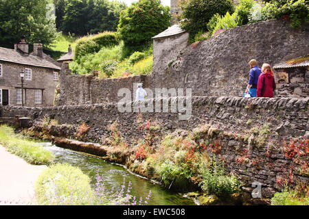 Wanderer passieren einer Trockensteinmauer auf Peakshole Wasser im Herzen von Castleton Dorf im Sommer Peak District Derbyshire UK Stockfoto