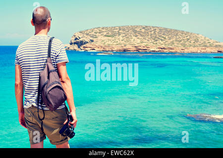 ein junger kaukasischen Mann mit einer Kamera in der Hand, Blick auf das Meer und die Insel Illa des Bosc in Insel Ibiza, Spanien Stockfoto