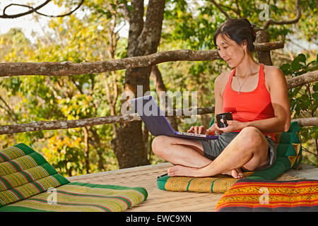 Frau sitzt mit ihrem Laptop auf einer Outdoor-Terrasse in einem Straßencafé in Nordthailand Stockfoto