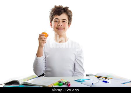 Kaukasische Teenager junge hält eine Mandarine mit rechten Hand während der Hausaufgaben Stockfoto