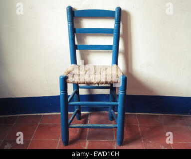 Alte blaue Holzstuhl mit geflochtenen Sitz steht in leeren Innenraum, weiße Wand und roten Boden Fliesen. Vintage-Stil. Foto mit Ton Stockfoto