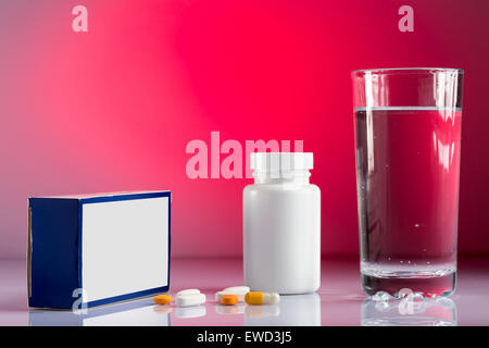 Verschiedene Pillen, Box, Flasche und Glas Wasser auf farbigen Hintergrund Stockfoto