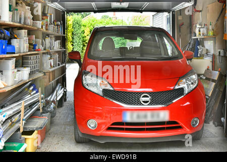 Fahrzeug in der Garage neben dem Wohngrundstück Red Nissan Auto geparkt Regallagerung von verschiedenen Haushaltsartikeln und Werkzeugen Essex England UK Stockfoto