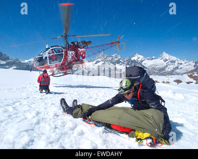 Mountain Rescue Personal trägt dazu bei, dass ein verletzter Bergsteiger in den Schweizer Alpen. Ein Sanitäter deckt den Patienten zum Schutz Stockfoto