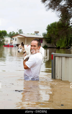 Ein älterer Mann sein geliebten Hund während einer Überschwemmung speichern und anzeigen überflutet Elemente im Hintergrund. Stockfoto