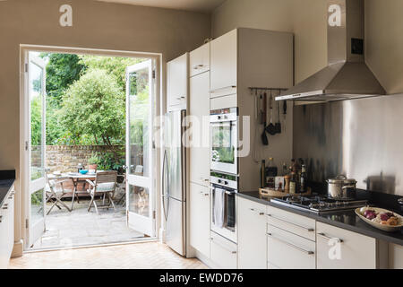 Französische Fenster öffnen auf Garten von Küche mit Küchengeräten aus Edelstahl und Granit-Arbeitsflächen Stockfoto