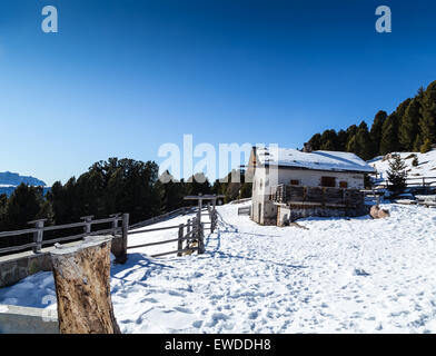 Alphütte, umgeben von einem Zaun im Schnee vor dem Panorama der schneebedeckten Gipfeln an einem sonnigen Tag im winter Stockfoto