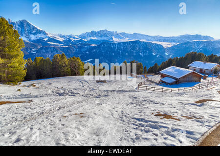 Alphütte, umgeben von einem Zaun im Schnee vor dem Panorama der schneebedeckten Gipfeln an einem sonnigen Tag im Winter auf Dolomiten Alpen Stockfoto